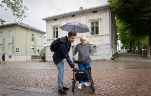 Vapaaehtoistoimija auttaa ikäihmisen tien yli.